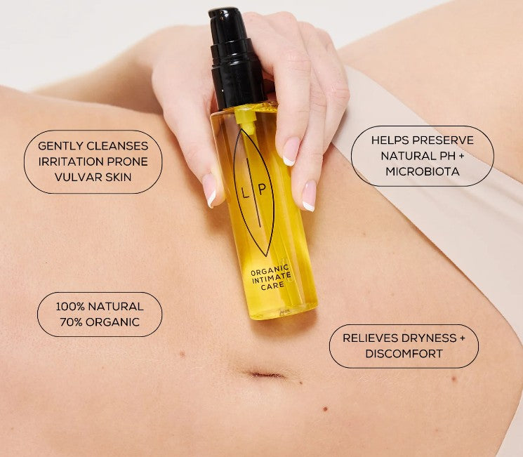 Hand holding a bottle labeled 'L.P.' over skin with product features text  
overlay. Organic Intimate Care. Gently cleanses irritation prone vulvar skin.